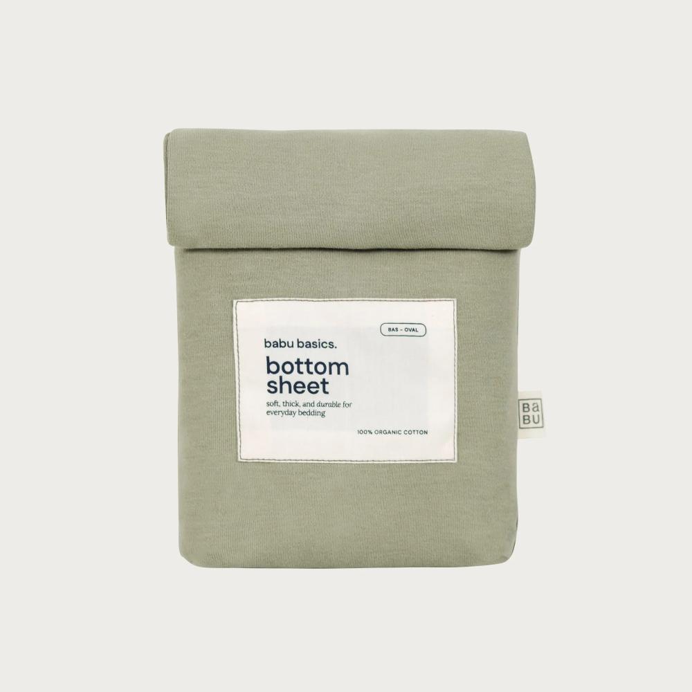 A sage green bottom sheet by babu basics, neatly folded and packaged in a matching fabric sleeve with a white label, set against a light gray background.