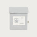 A light gray cotton bottom sheet by babu basics, neatly folded and packaged in a matching fabric sleeve with a white label, set against a solid off-white background.