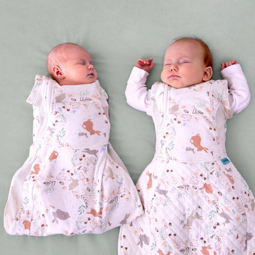 Two babies wearing patterned sleep sacks on a plain background showing the arms in and out in the purflo swaddle bag