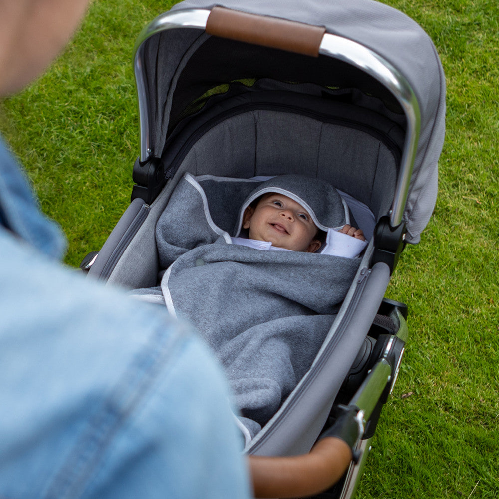 Baby in a stroller with a Purflo gray winter travel blanket, standing on grass
