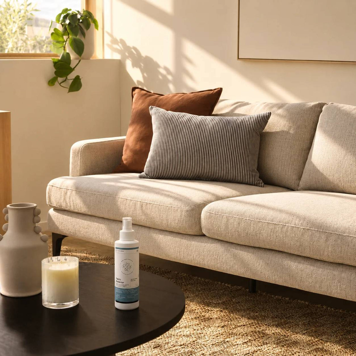Living room with a beige sofa, decorative pillows, a candle, and a bottle of fabric protector on a side table.