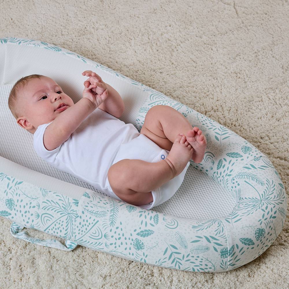 Baby lying on a floral-patterned baby nest on a carpeted floor