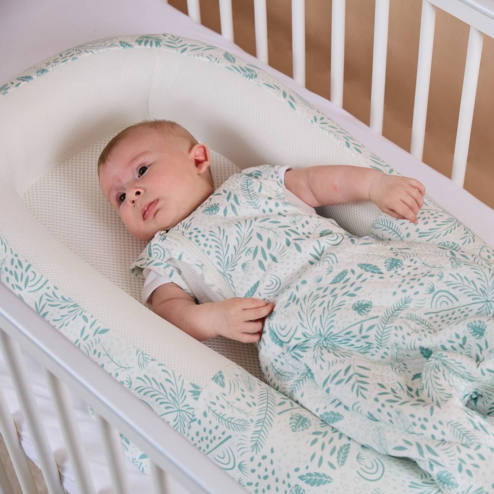 Baby lying in a breathable baby nest pod with a floral-patterned blanket