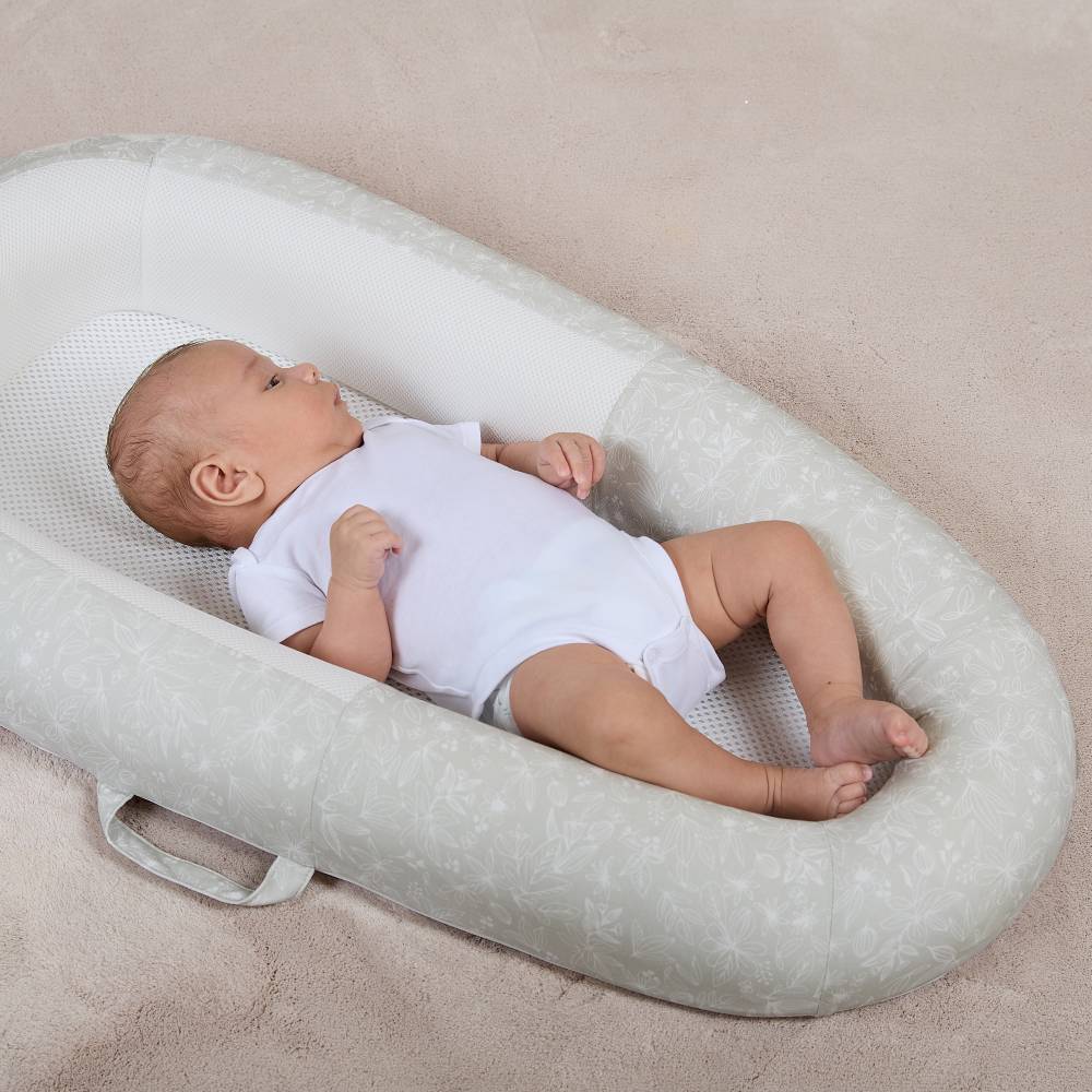 Baby lying in a soft, green Purflo Sleep Tight baby nest on a beige surface