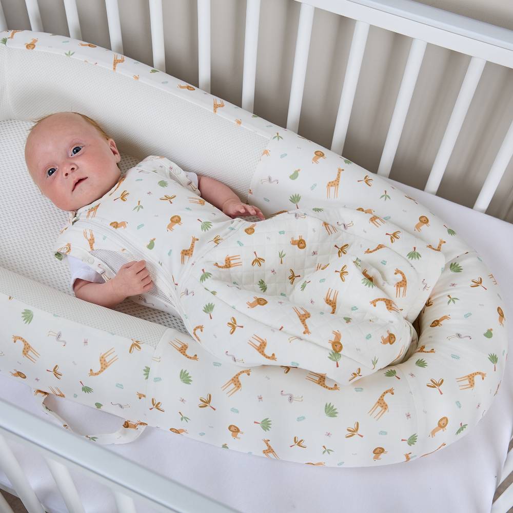 Baby wrapped in a swaddle with animal patterns in a firm sided mesh base nest in a cot
