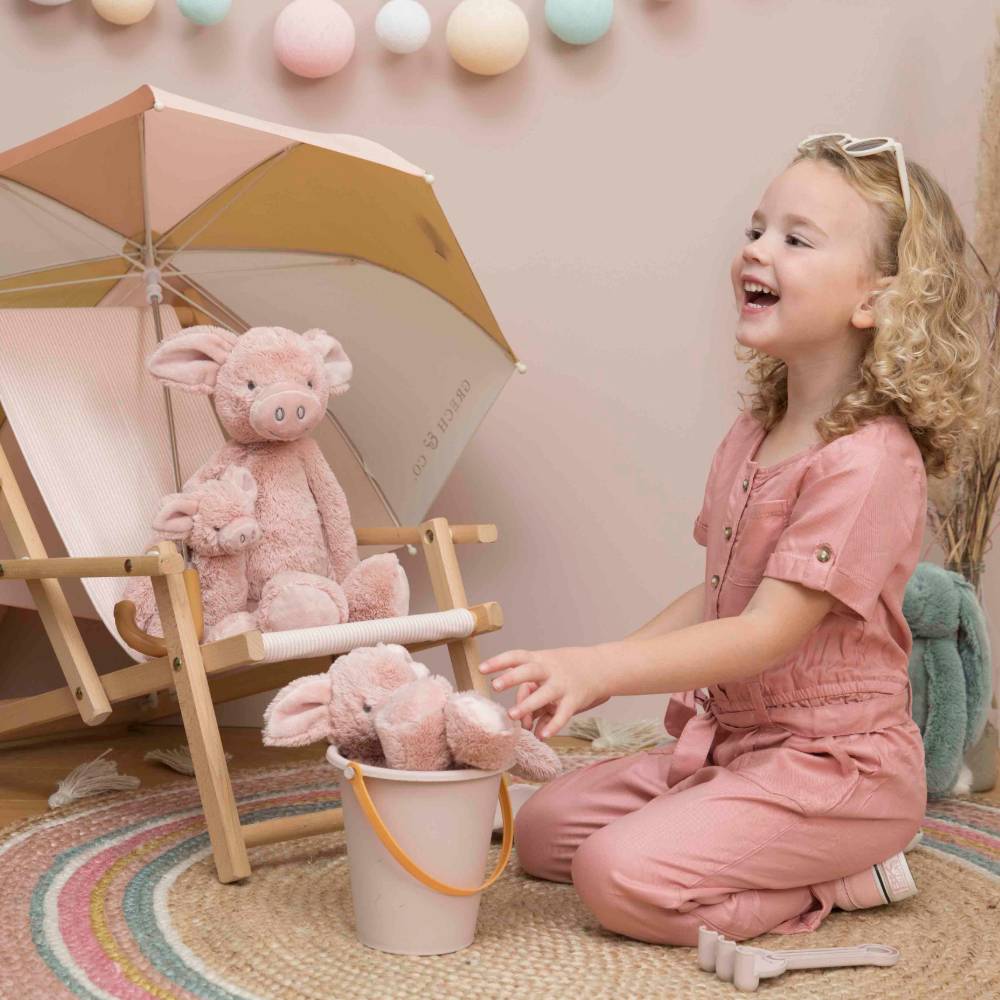 A young girl sitting down, smiling and playing with a group of Happy Horse Pig Perry soft toys. 