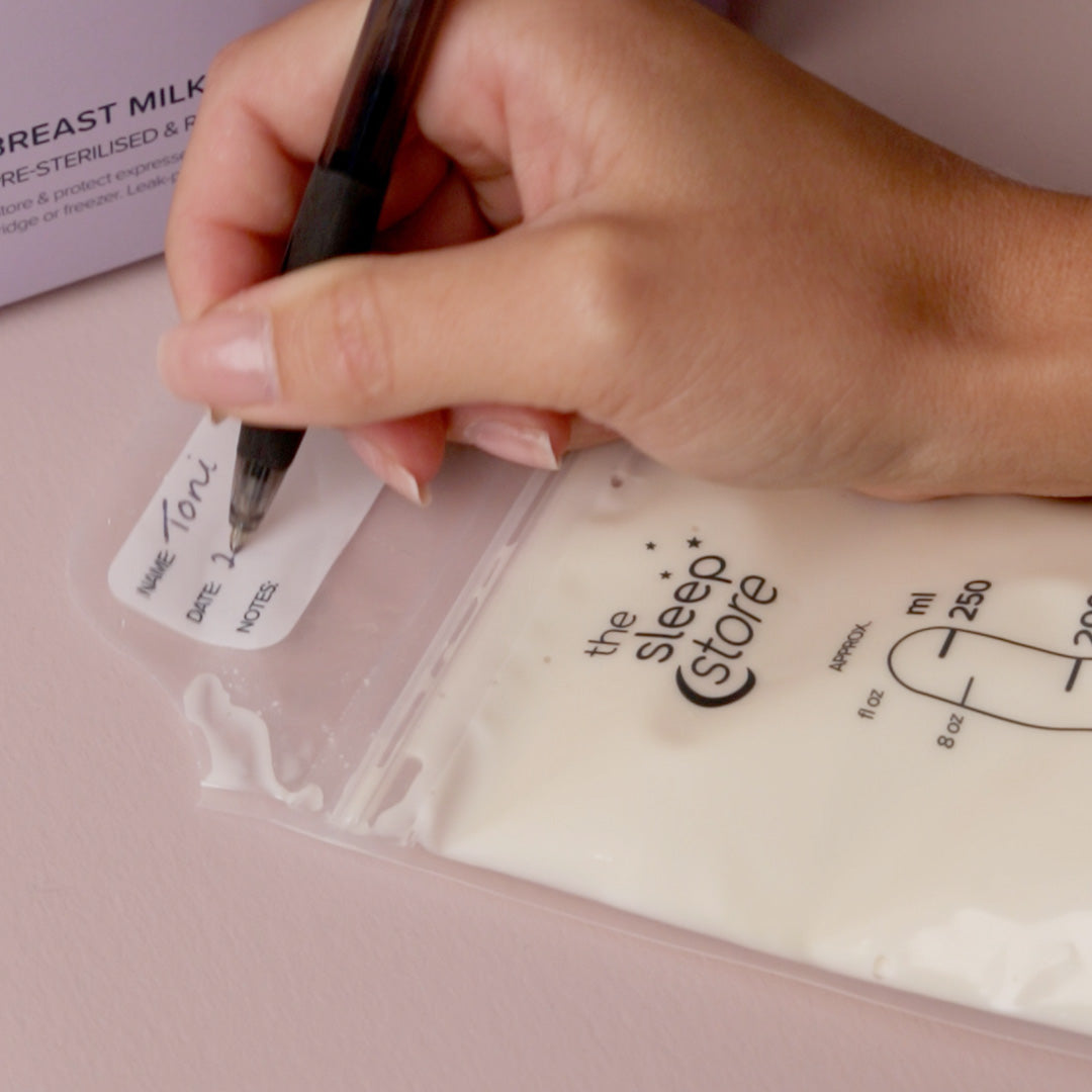 Hand writing on a label with 'the sleep store' branding next to a breast milk storage bag.