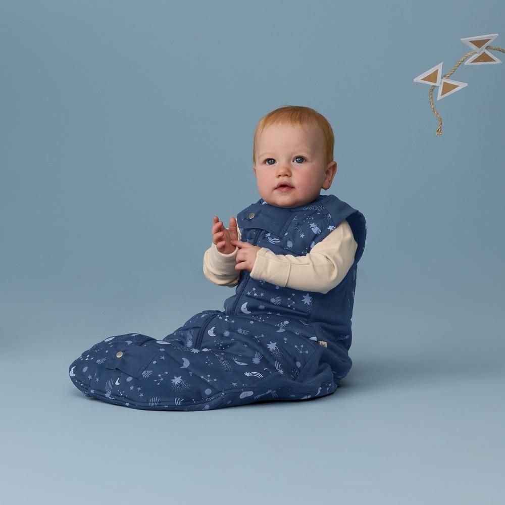 baby sitting in a navy blue sleep sack with blue background