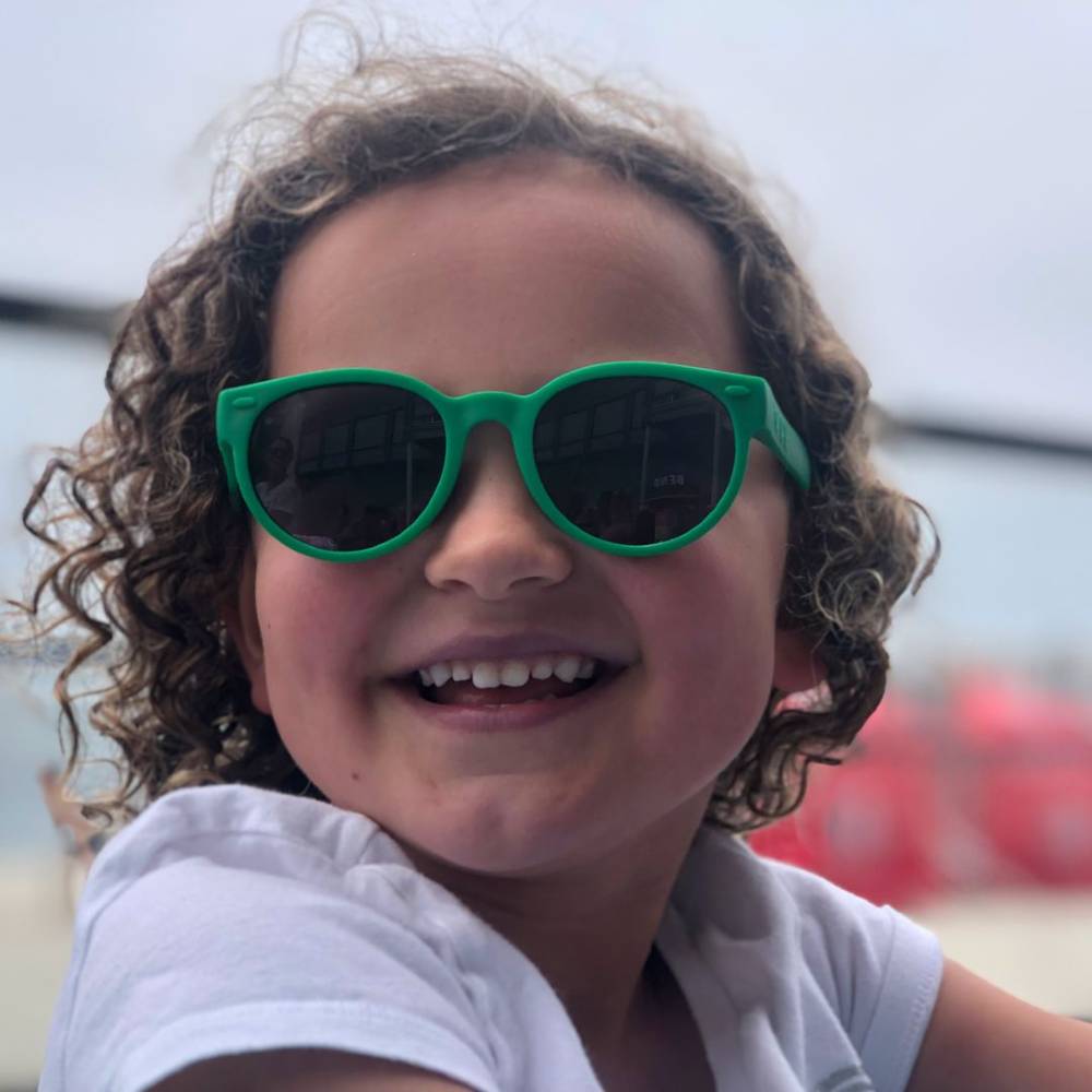 Child wearing round green ro.sham.bo sunglasses with a blurred background

