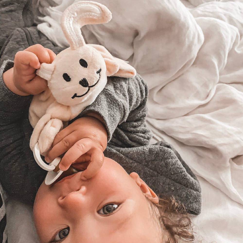 Baby holding beige bunny Sleepytot comforter.