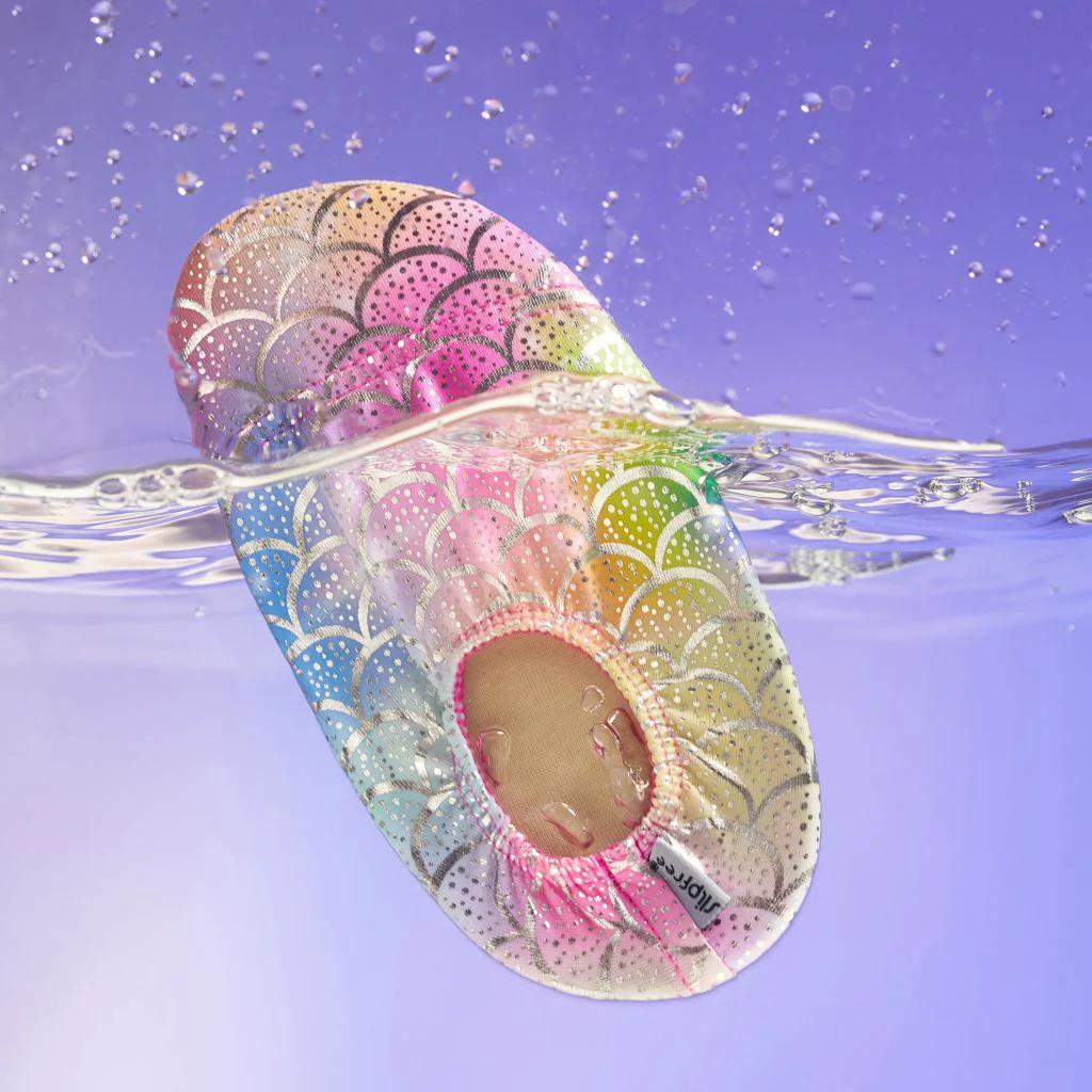 Colorful metallic mermaid scale-patterned slipfree water shoes partially submerged in water with a purple gradient background.