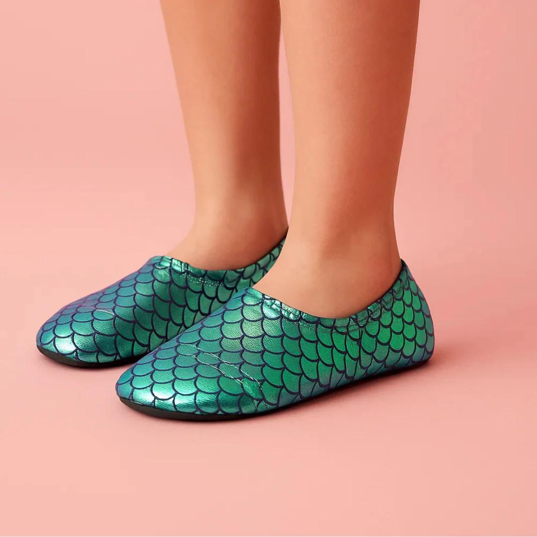 child wearing metalllic green mermaid scale patterned slipfree shoes on a pink background