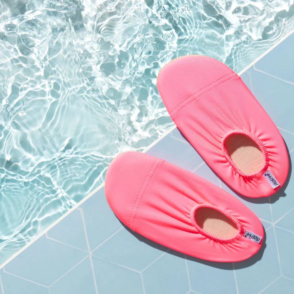 Pair of neon pink slipfree water shoes on a poolside surface with water in the background
