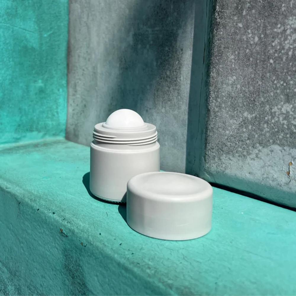 Grey sunscreen container with ball on a textured teal surface