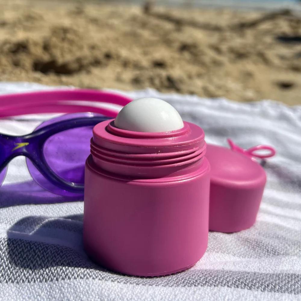 Pink suncreen container with a white ball on a beach towel.