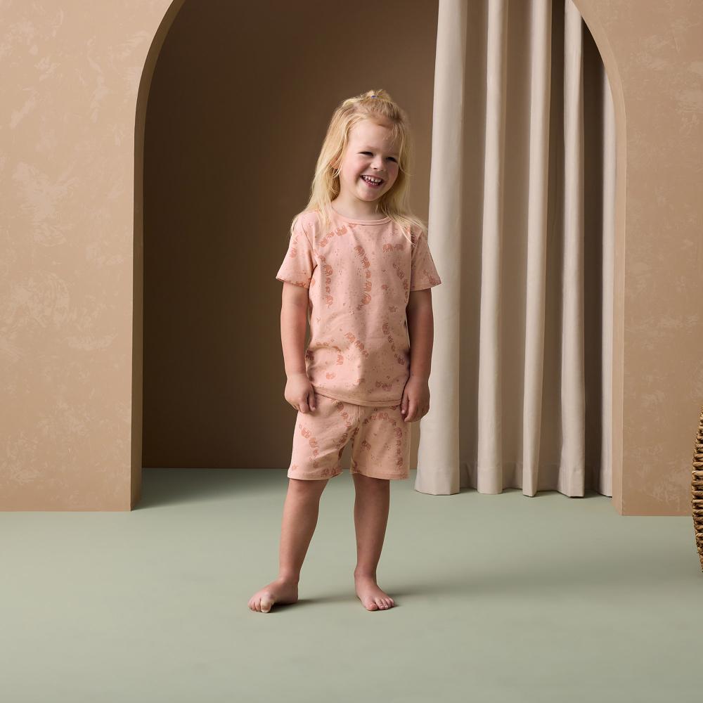 Young girl in a pink elephant print pyjamas standing in a minimalistic room with beige walls and green floor.