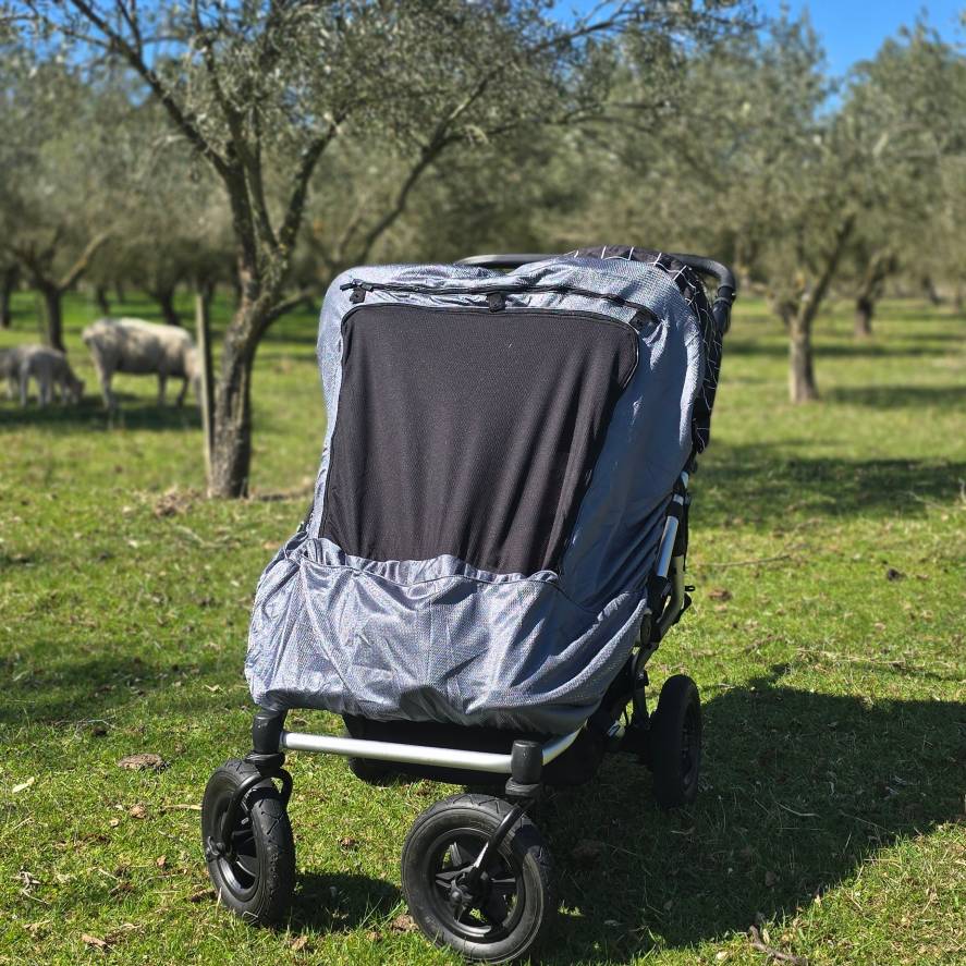 Twin stroller with a Snoozeshade blackout cover in an outdoor setting with trees and sheep in the background