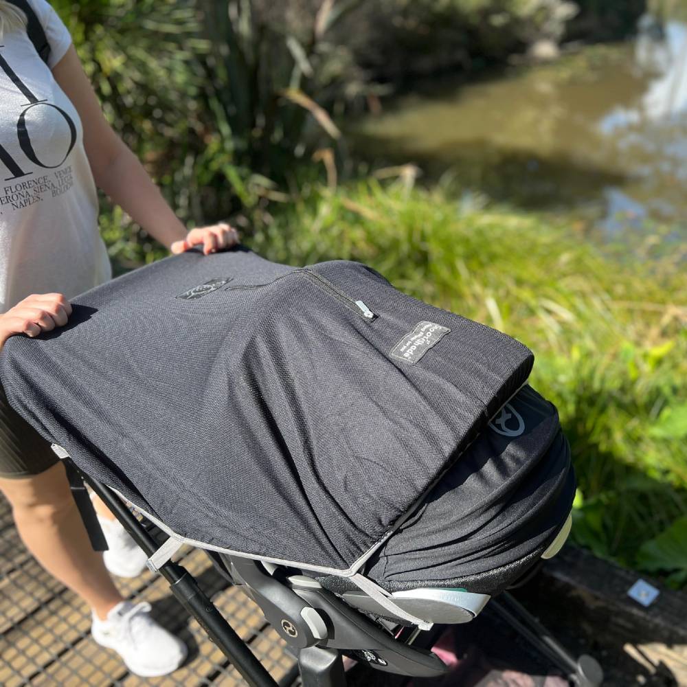 Person pushing a baby stroller with a Snoozeshade cover with a blurred natural background