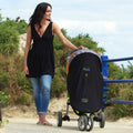 Woman pushing a stroller with a black Snoozeshade cover outdoors on a sunny day.