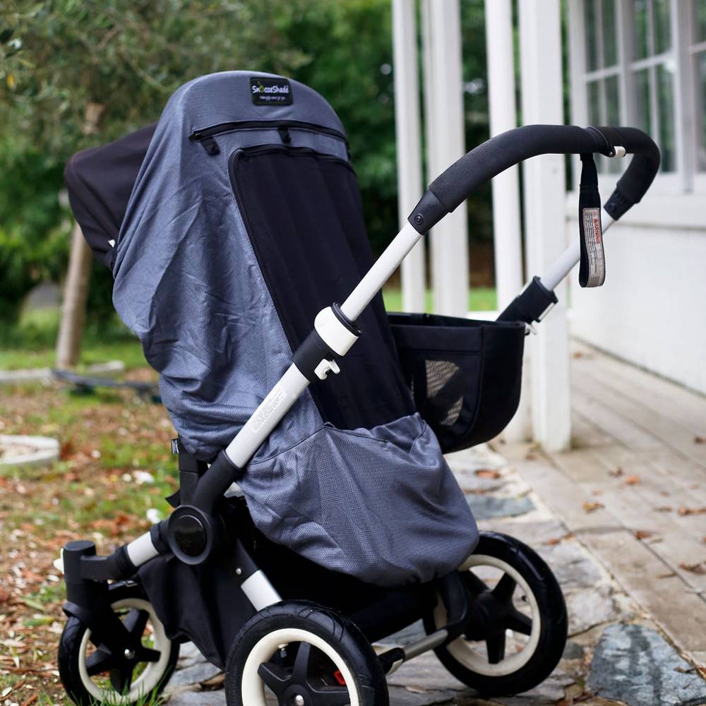 Black and silver stroller with a gray Snoozeshade cover on a stone path outdoors.