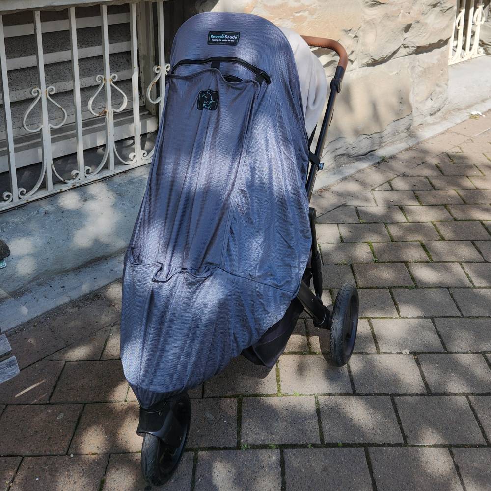 Stroller covered with a grey SnoozeShade blackout cover on a sidewalk.