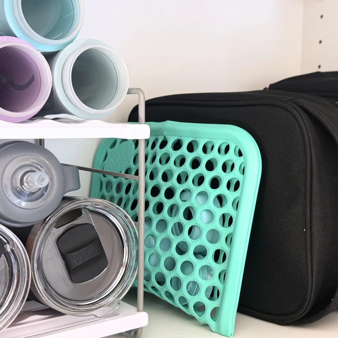 Turquoise silicone mesh cleaning pouch on a storage shelf with colorful food bottles and a black bag.