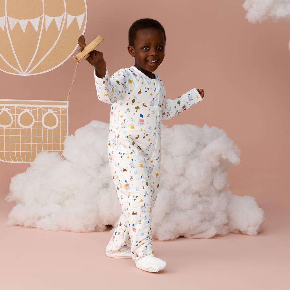 Child in a patterned onesie standing in front of a cloud and hot air balloon decoration on a pink background