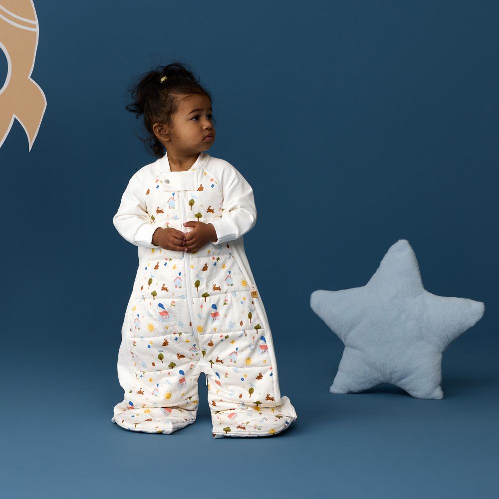 Child wearing a white onesie with colorful patterns, standing against a blue background with a star-shaped pillow.