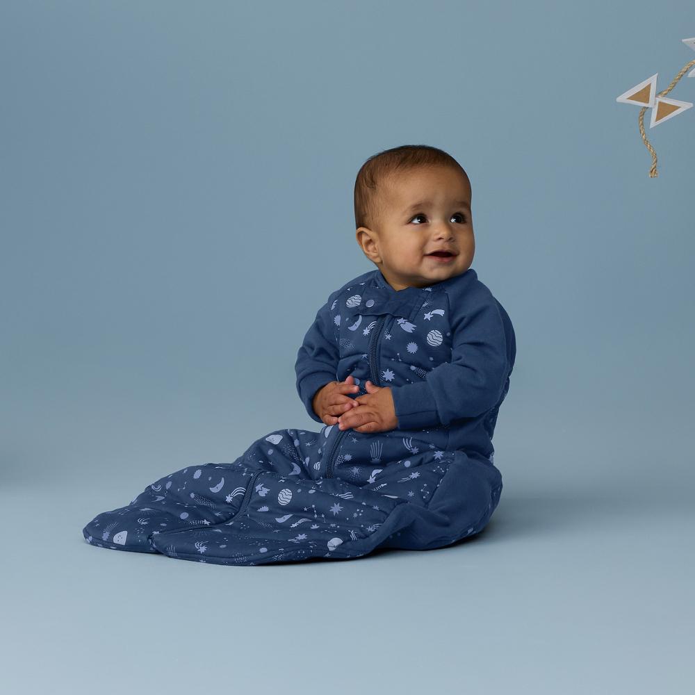 Baby in a blue onesie with star pattern sitting on a light blue background