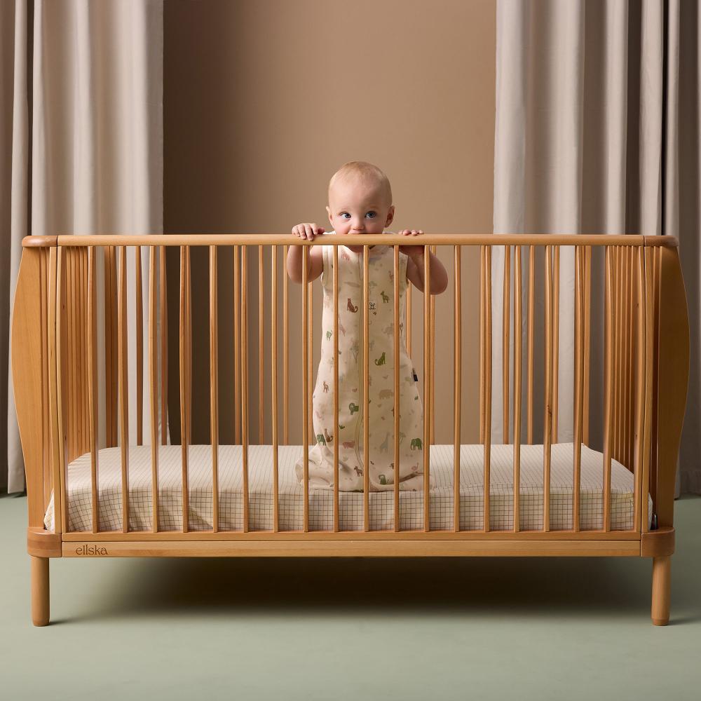 Baby standing in a wooden crib with a neutral background