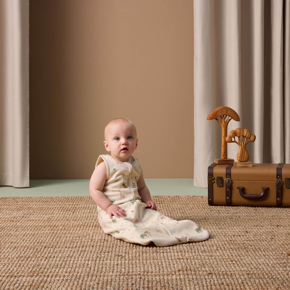 Baby sitting on a textured floor with a suitcase and wooden toys in the background.