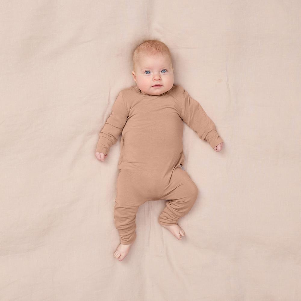 Baby wearing a brown onesie lying on a beige blanket