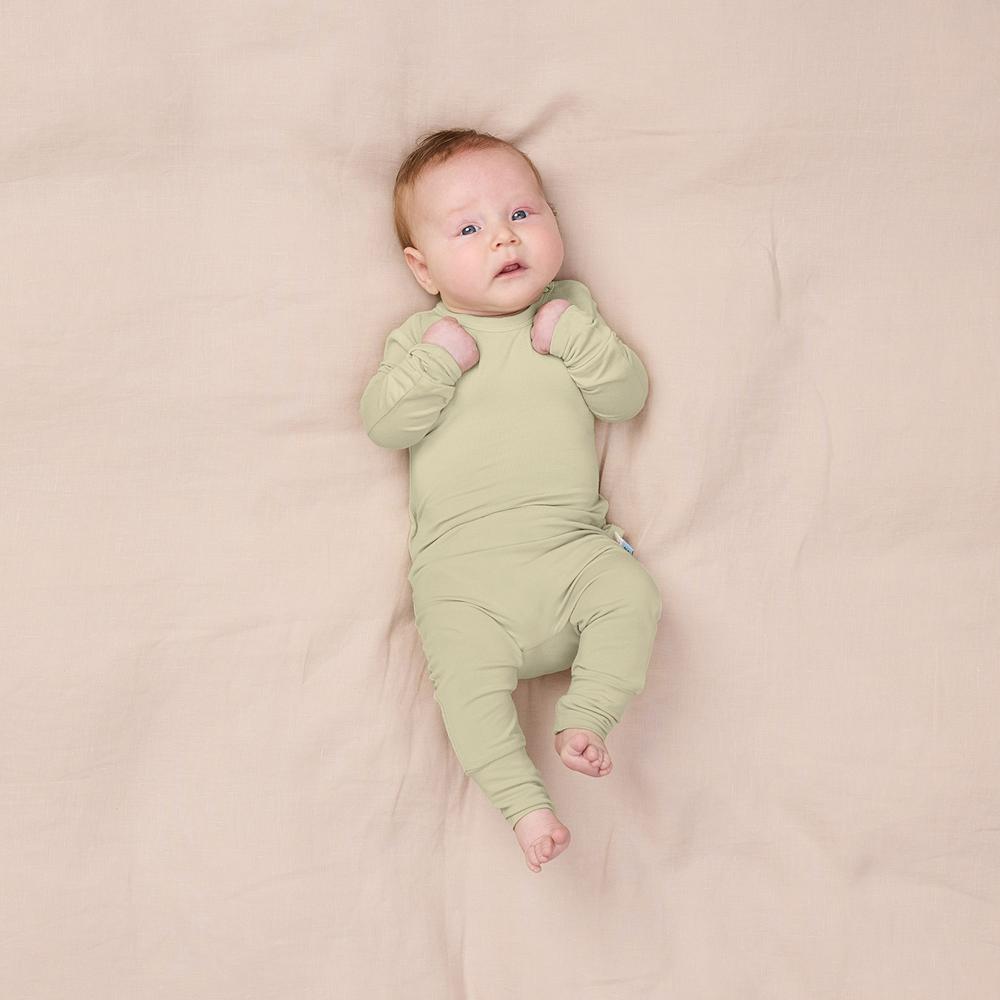 Baby wearing a green onesie lying on a beige blanket