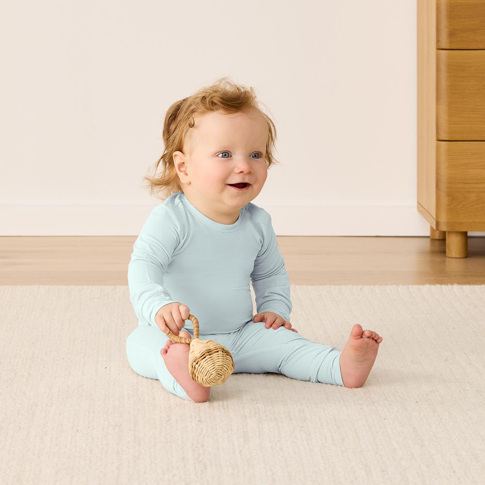 Baby in light blue outfit sitting on a beige carpet with a wooden toy.