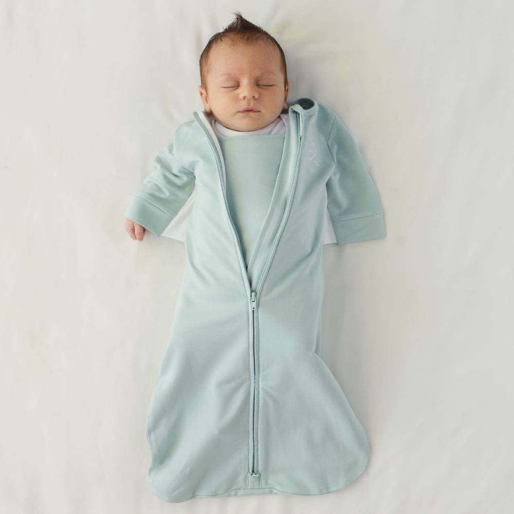 Baby wearing green Butterfly swaddle against white background.