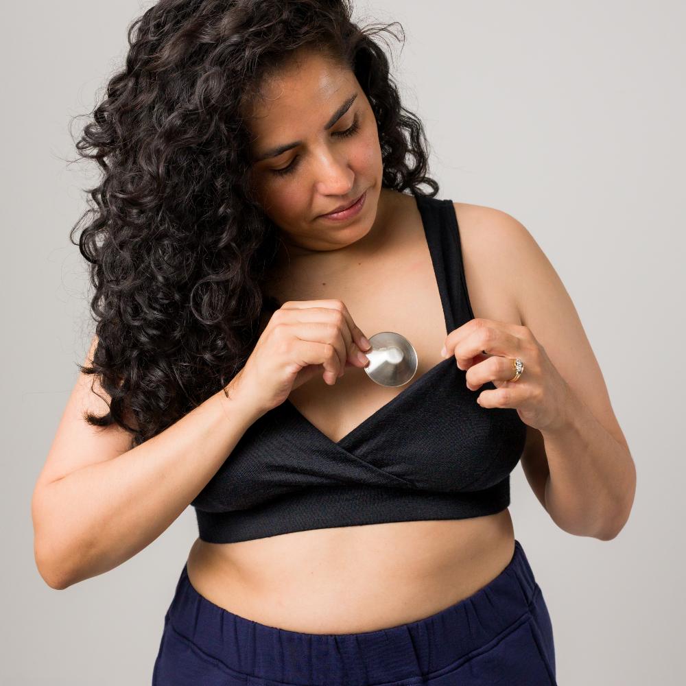 Woman holding a silver nipple cup to her chest against a plain background