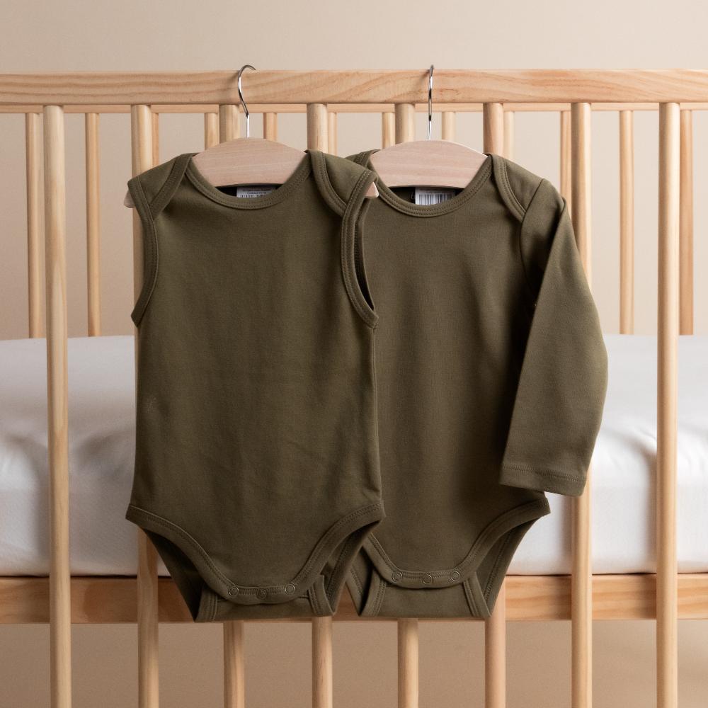 Two organic cotton green baby bodysuits on hangers against a wooden crib background