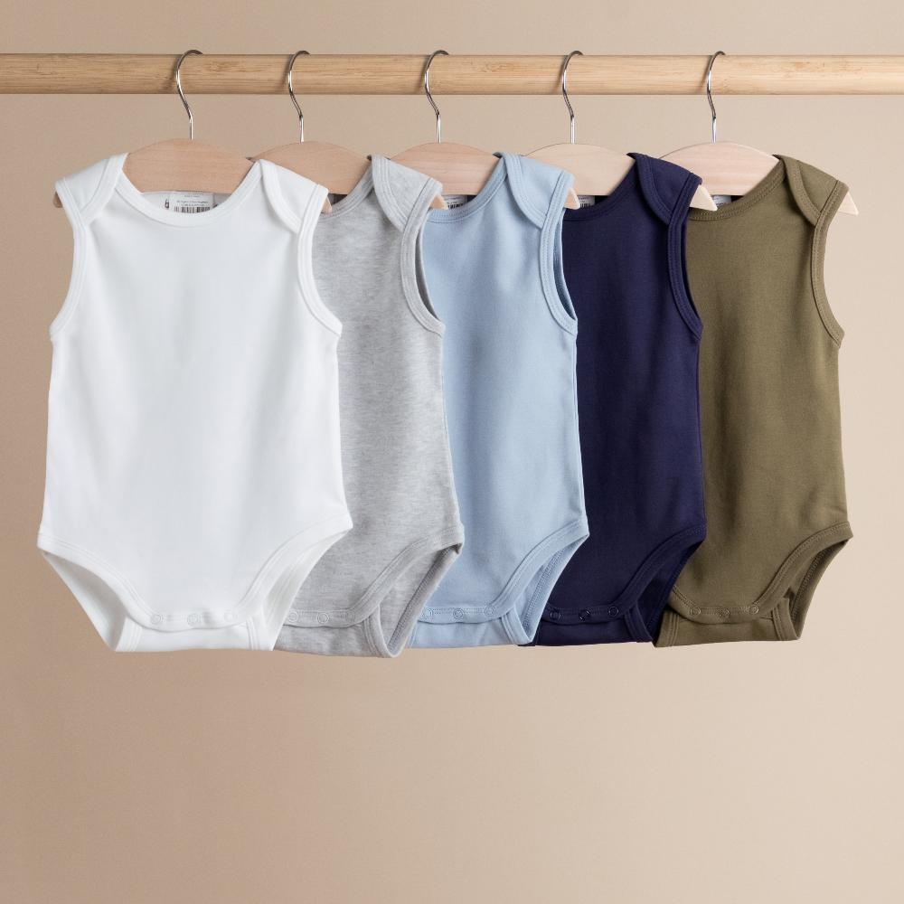 Five sleeveless baby singletsuits in different colors hanging on a wooden rod against a beige background.