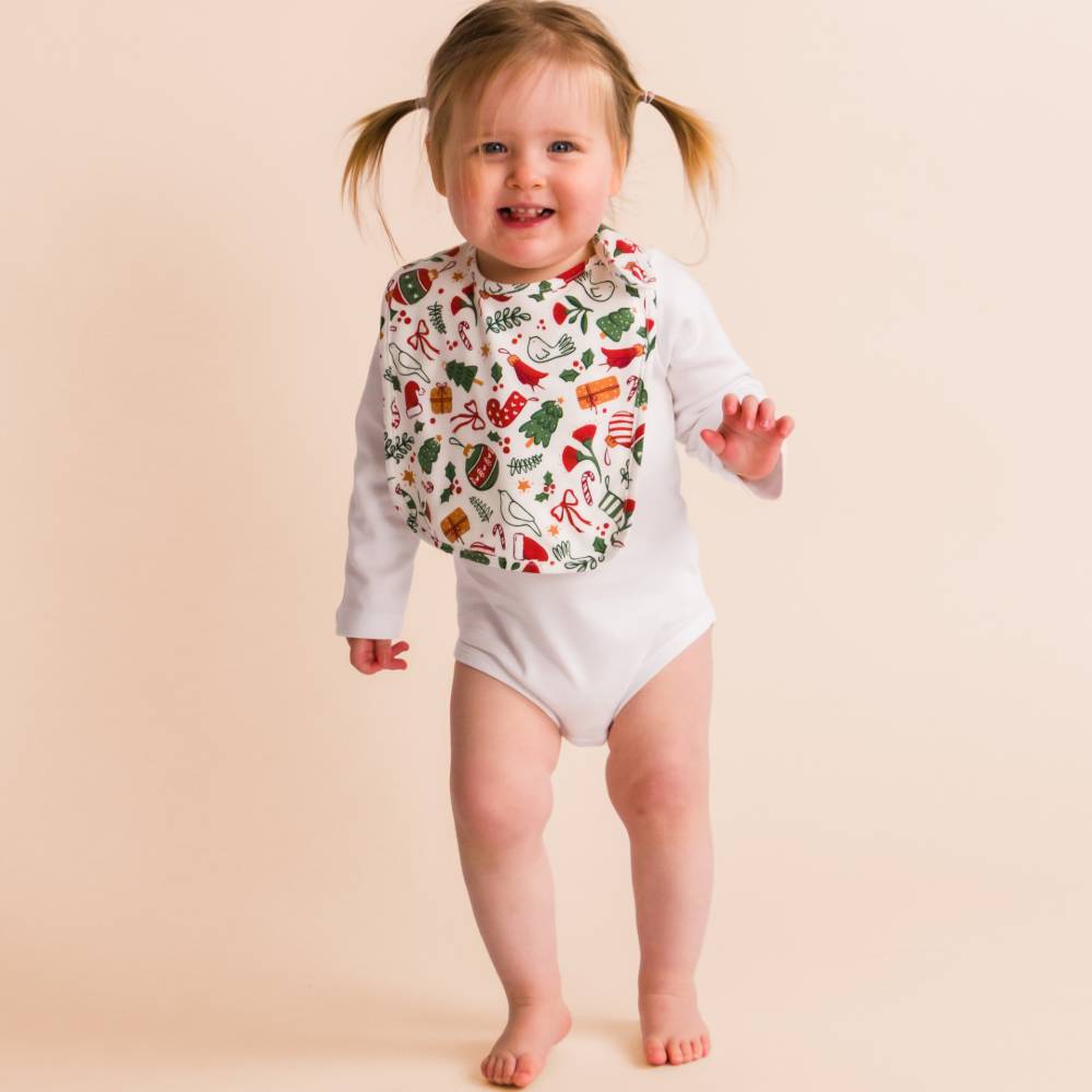 Child wearing a colorful christmas bib with a pattern on a beige background