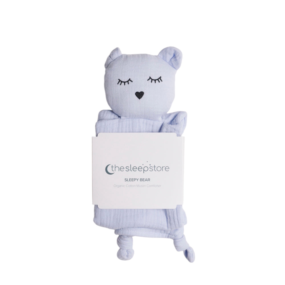 Blue stuffed bear comforter with a heart nose and closed eyes, wrapped in a blanket with 'the sleep store' branding on a white background.