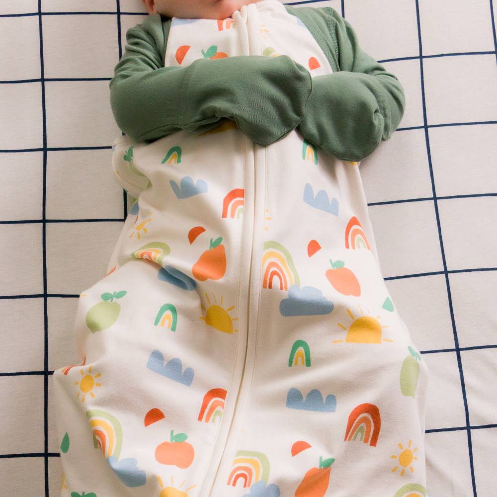 Baby in a colorful onesie with rainbow and cloud patterns on a checkered background