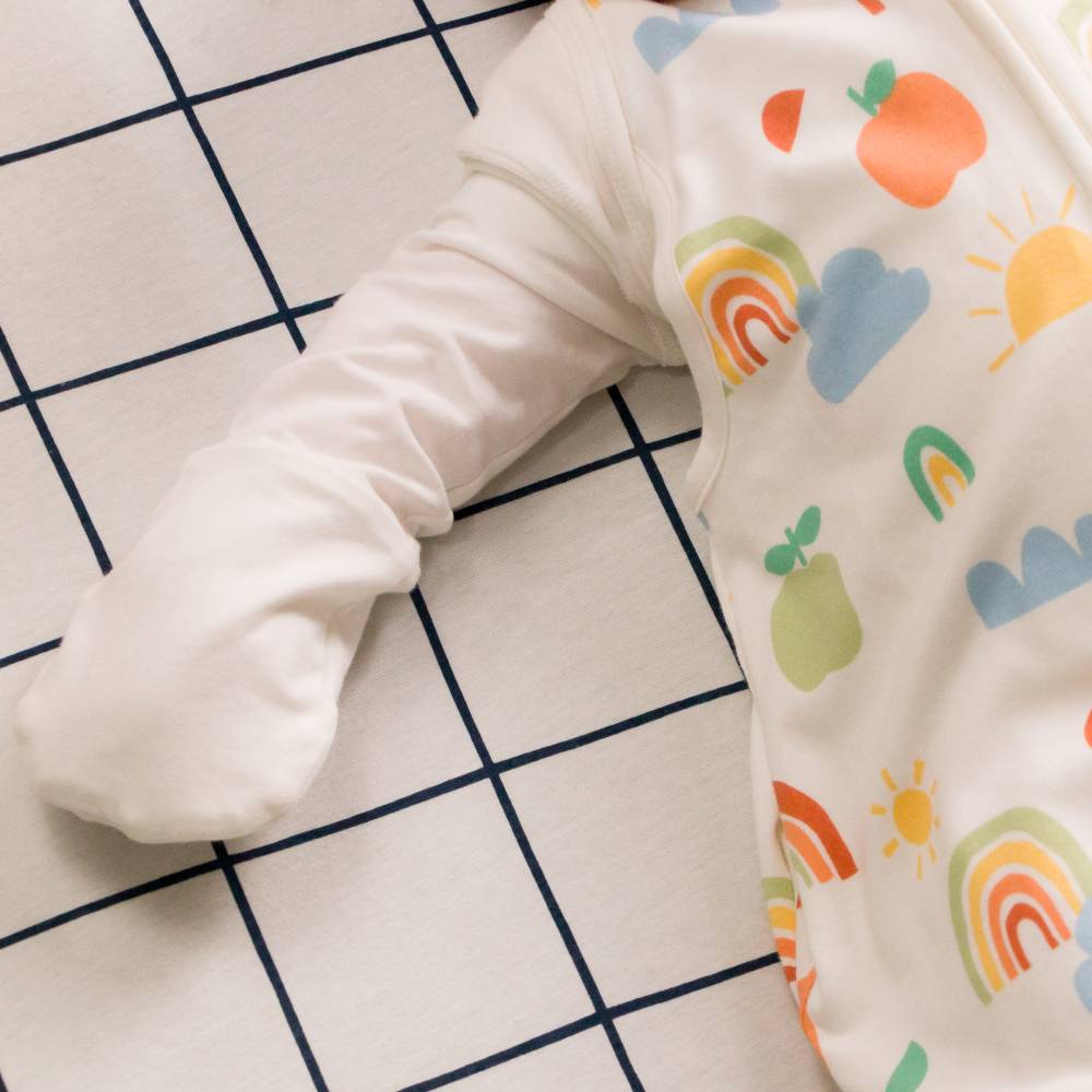 Baby's arm wearing a colorful patterned sleeping bag and white cotton long sleeve mittens on a grid background