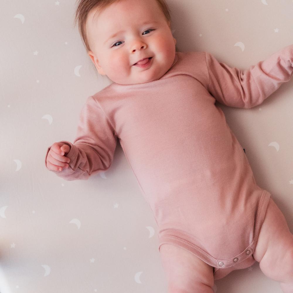 Baby in a pink onesie lying on a light-colored surface with a subtle pattern.