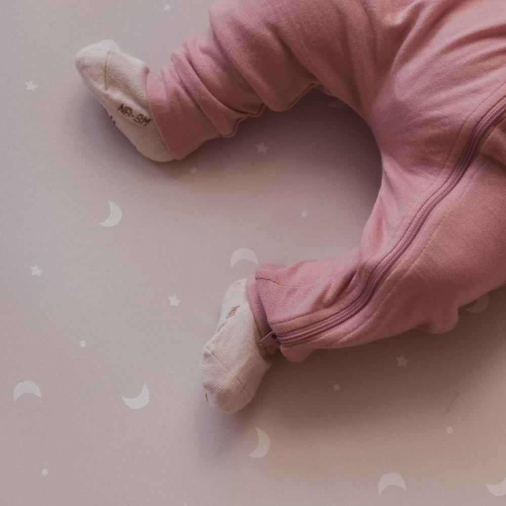 Baby in pink merino zip onesie on a light pink surface with subtle patterns