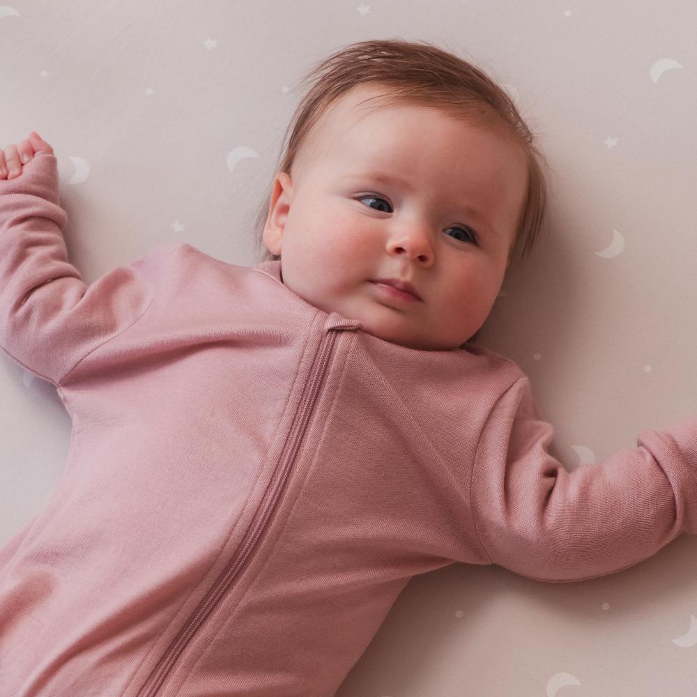 Baby wearing a pink merino onesie lying on a soft surface with a star-patterned blanket.