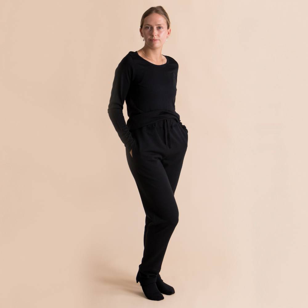 A woman modeling a black long-sleeve top and matching black drawstring sweatpants in merino fleece against a solid beige studio background.