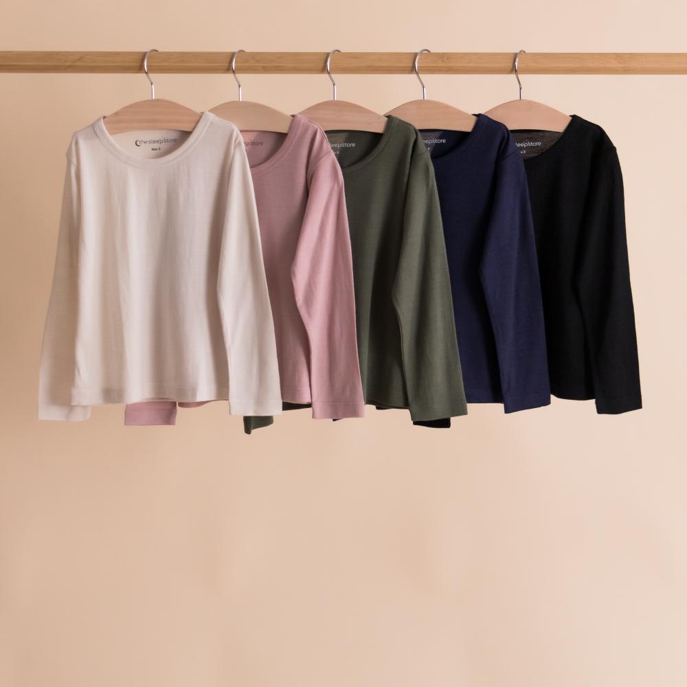 Five long-sleeve shirts in different colors hanging on a rack against a beige background.