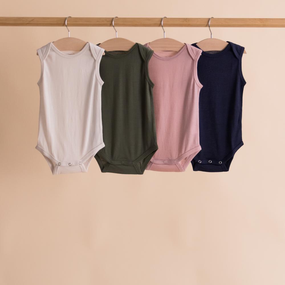 Four sleeveless baby singletsuits in white, green, pink, and navy hanging on a rack against a beige background.