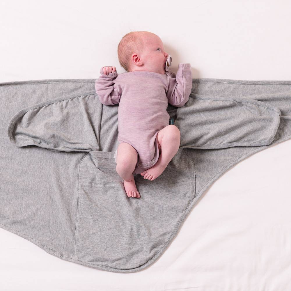 Newborn baby in a pink merino onesie lying on a grey miracle blanket swaddle on a white background 