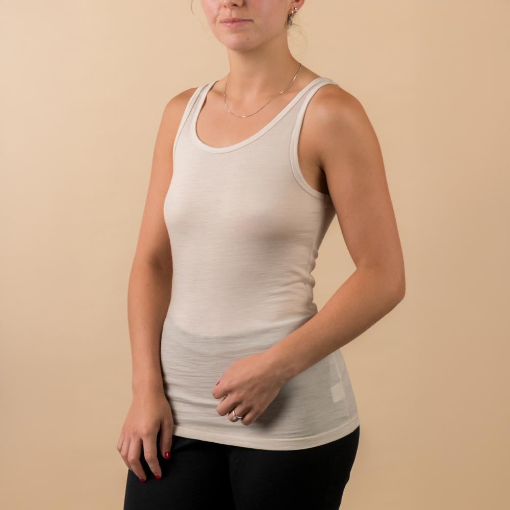 A woman wearing a white tank top and black pants, standing against a solid beige background.
